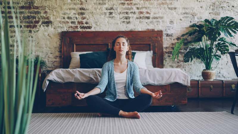 Minimalist illustration of a seated person meditating quietly beside a smartphone displaying a calm blue Buddhify-style app interface, soft natural light background